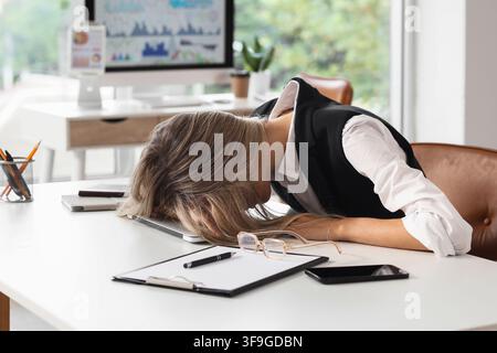 Donna d'affari esausta che dorme sul laptop alla scrivania dell'ufficio, concetto di burnout e sovraccarico, stress e stanchezza nell'ambiente aziendale Foto Stock