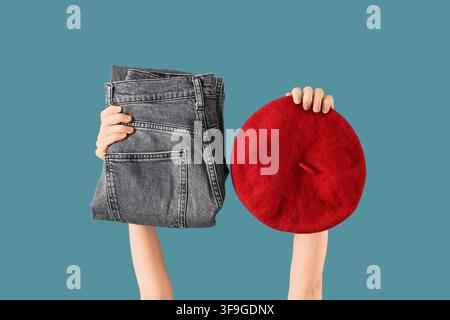 Mani che tengono jeans grigi piegati e un berretto rosso, concetto di moda e scelta stilistica, abbigliamento e accessorio casual Foto Stock