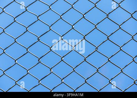 Una vista ravvicinata di una recinzione in maglia di ferro contro un cielo blu chiaro. La recinzione presenta un motivo a rombo con fili metallici che creano uno sfondo testurizzato Foto Stock