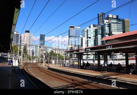 I pendolari attendono sul binario della stazione ferroviaria di Roma Street con lo skyline moderno della città che si erge dietro di loro a Brisbane, Queensland, Australia Foto Stock
