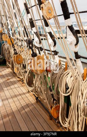 Vista verticale di sartie, carrucole di legno e sartie arrotolate sul ponte di una barca a vela, attrezzatura nautica Foto Stock