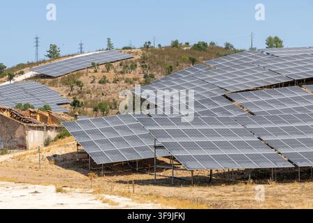 File di pannelli fotovoltaici sono installati su una collina arida dal sole, con alcune strutture più vecchie visibili nelle vicinanze Foto Stock