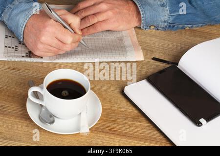 Uomo che lavora alla sua scrivania con un giornale, una tazza di caffè e un quaderno Foto Stock