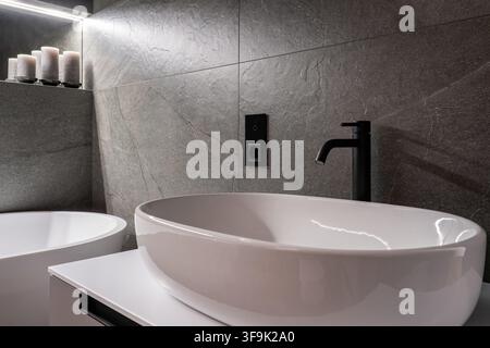 Lavandino ovale moderno con rubinetto nero su parete di piastrelle in pietra, interno di bagno lussuoso, dettaglio di design di bagno spa contemporaneo Foto Stock