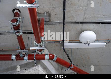 Protezione antincendio moderna e infrastrutture di servizio con tubi sprinkler rossi, condotti elettrici e sistemi meccanici montati a soffitto Foto Stock