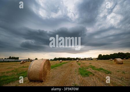 Cielo drammatico su un campo raccolto con balle di fieno rotonde prima dell'arrivo di una tempesta nella Val Padana, Nord Italia Foto Stock