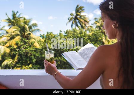 Donna legge un libro e tiene una bevanda fredda su un balcone alle Maldive Foto Stock