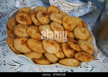 Uno scatto ad angolo laterale di un vassoio ricolmo di piccole torte rotonde di formaggio greco fritte (tyropitakia) su un tavolo da buffet allestito con pentole tradizionali. Foto Stock