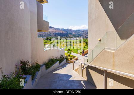 Bellissima vista di un vialetto moderno del resort tra edifici con giardini e montagne. Creta. Grecia. Foto Stock