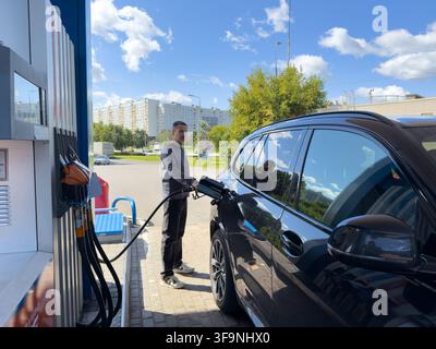 Mosca, Russia – 14 agosto 2026: Primo piano di un uomo che fa il pieno a un’auto, mostrando l’ugello della pompa benzina inserito nel serbatoio del veicolo. Foto Stock