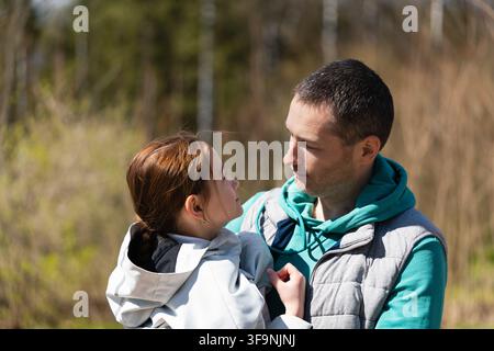Padre felice che tiene in braccio sua figlia di 7-8 anni all'aperto. Si guardano e sorridono. Foto Stock