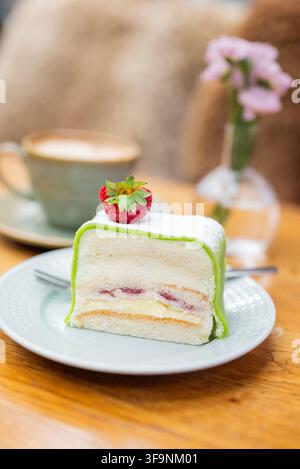 Fetta di tradizionale torta principessa svedese con marzapane verde, panna montata, pan di Spagna e ripieno di frutti di bosco, guarnita con una fragola fresca e servita con c Foto Stock