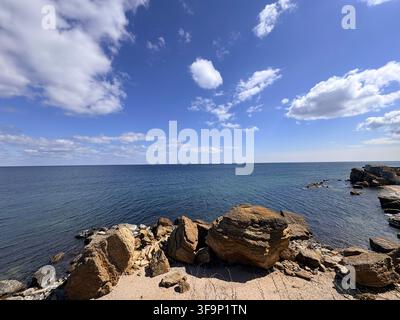 Splendido paesaggio costiero caratterizzato da grandi massi su una spiaggia sabbiosa contro un mare blu profondo e un vivace cielo soleggiato. Foto Stock