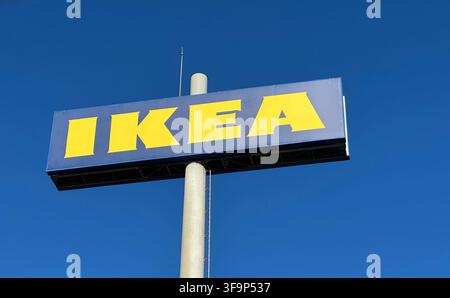 Chiarissima ripresa a bassa angolazione esterna di un grande e prominente cartello IKEA con lettere gialle brillanti su un pannello rettangolare blu montato su un alto pilastro di cemento Foto Stock