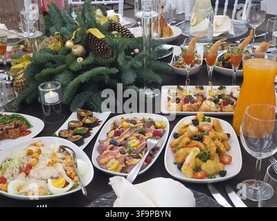 Un tavolo da banchetto festivo apparecchiato con un ricco buffet natalizio. Il centrotavola presenta rami di sempreverdi freschi decorati con pigne e oro Foto Stock