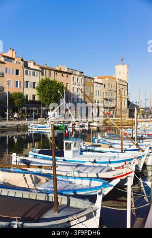 Barche da pesca tradizionali colorate ormeggiate nel vecchio porto di La Ciotat, Francia, con sullo sfondo edifici storici sul lungomare e un orologio torre. Foto Stock