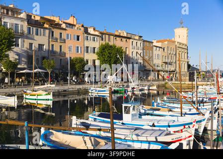 Le tradizionali barche Pointu costeggiano le acque calme del vecchio porto di La Ciotat, in Francia, con edifici storici e caffè lungo il molo. Foto Stock