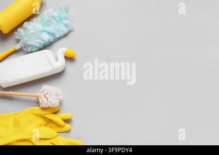 Prodotti per la pulizia della casa con guanti gialli, spazzolino per il bagno, spolverino e bottiglie di detersivo su uno sfondo grigio Foto Stock