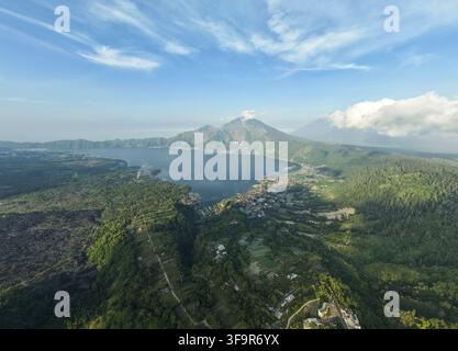 Vista aerea del Monte Abang che si affaccia sul Lago Batur con foreste rigogliose, terreno vulcanico e il villaggio di Kintamani, Bali, Indonesia. Foto Stock