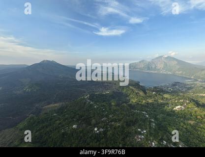 Vista aerea del Monte Batur e del Monte Abang che si affacciano sul sereno Lago Batur, circondati da un paesaggio vulcanico lussureggiante e da piccoli villaggi a Kintam Foto Stock