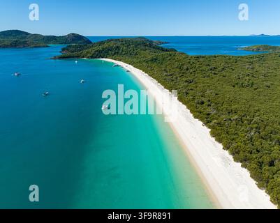 Vista aerea di Whitehaven Beach con la sua sabbia bianca incontaminata e l'acqua turchese circondata da una foresta lussureggiante e barche nelle Whitsunday Islands, Airlie Foto Stock