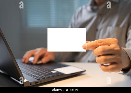 Primo piano di un professionista degli affari che tiene una carta bianca vuota accanto a un laptop, adatto per mockup, branding, pubblicità, identità, comunicazione d'ufficio Foto Stock