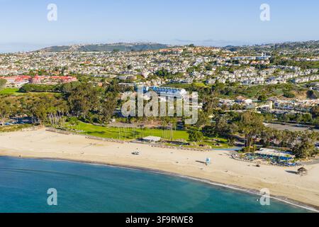 Vista aerea della spiaggia di Dana Point con una battigia sabbiosa, un parco verde, palme e case sui pendii che si affacciano sull'Oceano Pacifico a Dana P Foto Stock