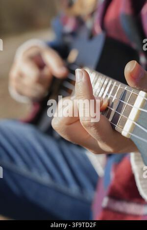 Primo piano di mani femminili che suonano chitarra ukulele all'aperto in una foresta autunnale. Concetto di terapia del suono, salute mentale e rituali di benessere. Calma tran Foto Stock