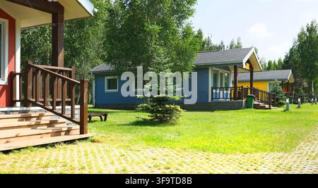 Scalini in legno della terrazza nel villaggio di cabine per le vacanze. Concetto di stile di vita lento ecoturistico all'aperto accogliente. Giardino del parco estivo tranquillo per la famiglia Foto Stock