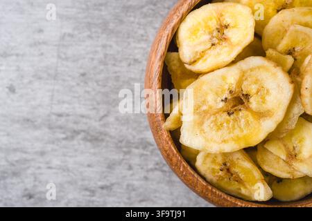 Chips di banana croccanti in una ciotola di legno su sfondo grigio Foto Stock