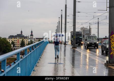 La pioggia è tornata: Inizio di settimana bagnato a Bonn Bonn, 17 agosto 2026 La pioggia è tornata a Bonn: Con l’ombrello aperto, un uomo attraversa il ponte Kennedy di Beuel in direzione del centro città di Bonn. La pioggia cade sul ponte, i sentieri e la strada sono bagnati e riflettono la luce grigia di una mattina piovosa. Dopo le settimane precedenti in parte asciutte e estive, il tempo si mostra di nuovo più variabile all’inizio della settimana. Il Servizio Meteorologico Tedesco segnala per lunedì una situazione meteorologica instabile con pioggia e temporali. Bonn Beuel Renania Settentrionale-Vestfalia Germania Foto Stock