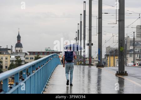 La pioggia è tornata: Inizio di settimana bagnato a Bonn Bonn, 17 agosto 2026 La pioggia è tornata a Bonn: Con l’ombrello aperto, un uomo attraversa il ponte Kennedy di Beuel in direzione del centro città di Bonn. La pioggia cade sul ponte, i sentieri e la strada sono bagnati e riflettono la luce grigia di una mattina piovosa. Dopo le settimane precedenti in parte asciutte e estive, il tempo si mostra di nuovo più variabile all’inizio della settimana. Il Servizio Meteorologico Tedesco segnala per lunedì una situazione meteorologica instabile con pioggia e temporali. Bonn Beuel Renania Settentrionale-Vestfalia Germania Foto Stock