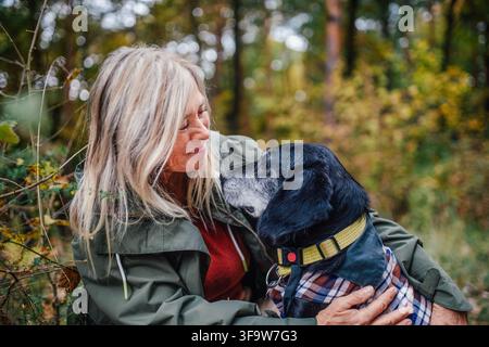 Donna anziana felice con il cane durante una passeggiata nella natura in una piovosa giornata autunnale. Foto Stock