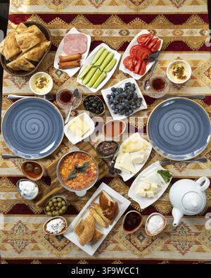 Una colazione turca vivace e invitante aspetta, completa di menemen, una varietà di formaggi, verdure fresche, olive, pane e ac tradizionale Foto Stock