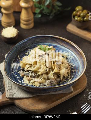 Pasta cremosa con pollo e funghi cosparsa di parmigiano grattugiato, servita in una ciotola di ceramica blu Foto Stock
