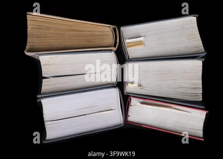 Un grande libro aperto sullo sfondo di una fila di pubblicazioni cartacee. Mucchio di vecchi libri e guide. Sfondo scuro Foto Stock