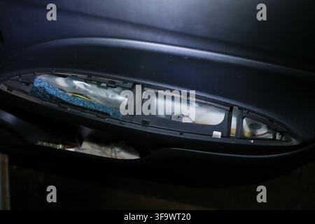 Un gruppo faro per veicolo in riparazione con componenti interni esposti, visto da vicino in un ambiente di garage buia, con involucro riflettente Foto Stock