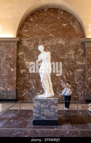 Turista che posa per una foto accanto alla Venere di Milo o Afrodite di Melos nella galleria delle antichità del Louvre a Parigi, Francia Foto Stock