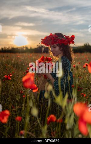 Ritratto di prato all'ora dorata con una giovane donna che indossa una corona di fiori di Papaver rhoeas e tiene papaveri rossi Foto Stock