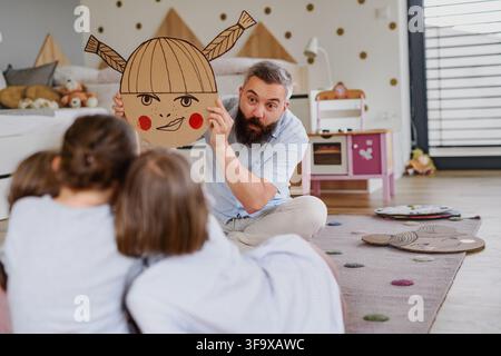Padre che insegna alle figlie le emozioni utilizzando espressioni facciali illustrate a casa. Foto Stock