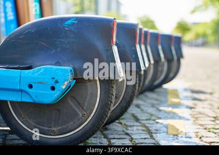 Filiera di scooter a noleggio parcheggiati su una strada di ciottoli, primo piano delle ruote posteriori e dei parafanghi. Condivisione di scooter elettrici in città Foto Stock