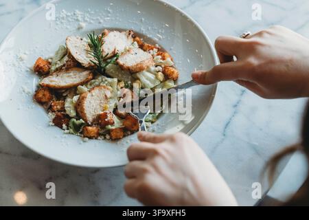 Donna che taglia pollo grigliato su un'insalata Caesar Foto Stock