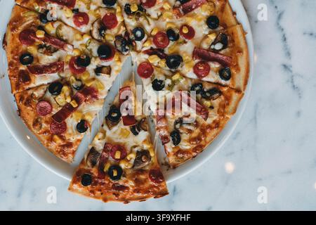 Pizza appena sfornata e affettata su un piano di lavoro in marmo Foto Stock