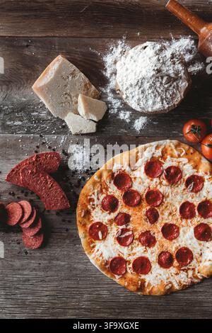 Pizza al pepperoni con ingredienti su un tavolo di legno rustico Foto Stock