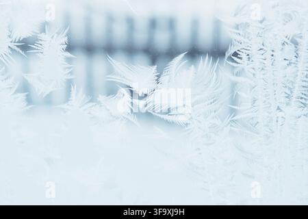 Bellissimi motivi ghiacciati su una finestra blu sullo sfondo di una recinzione Foto Stock