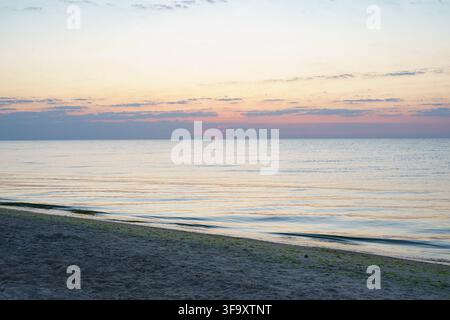 Bellissimo tramonto su un mare calmo e una spiaggia di sabbia con una calda luce dorata all'orizzonte. Foto Stock