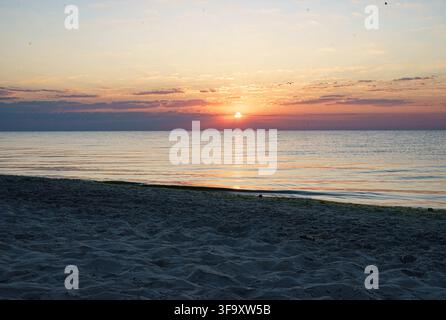 Bellissimo tramonto su un mare calmo e una spiaggia di sabbia con una calda luce dorata all'orizzonte. Foto Stock