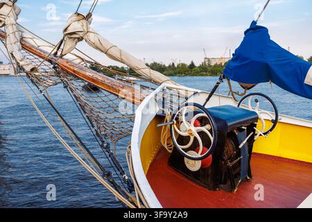 Una vista ravvicinata della prua di uno yacht vintage con un grande sperone di legno, reti di sartiame e un'antica verricello manuale per l'ancora. L'imbarcazione galleggia su un'acqua blu Foto Stock