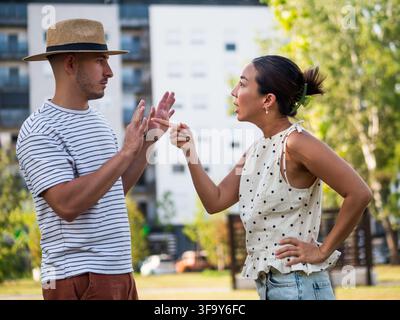 Donna che gesticola emotivamente verso il suo partner mentre lui alza le mani durante una conversazione tesa nel parco. Foto Stock