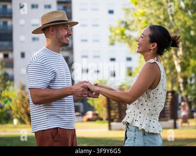 Uomo e donna sorridenti che condividono un abbraccio gioioso mentre godono di una bella giornata all'aperto. Foto Stock